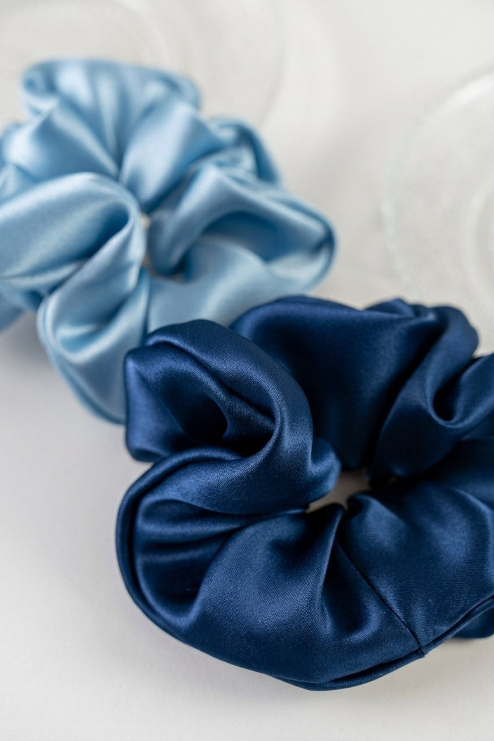 Two silk scrunchies, one blue and one navy, on a white background.