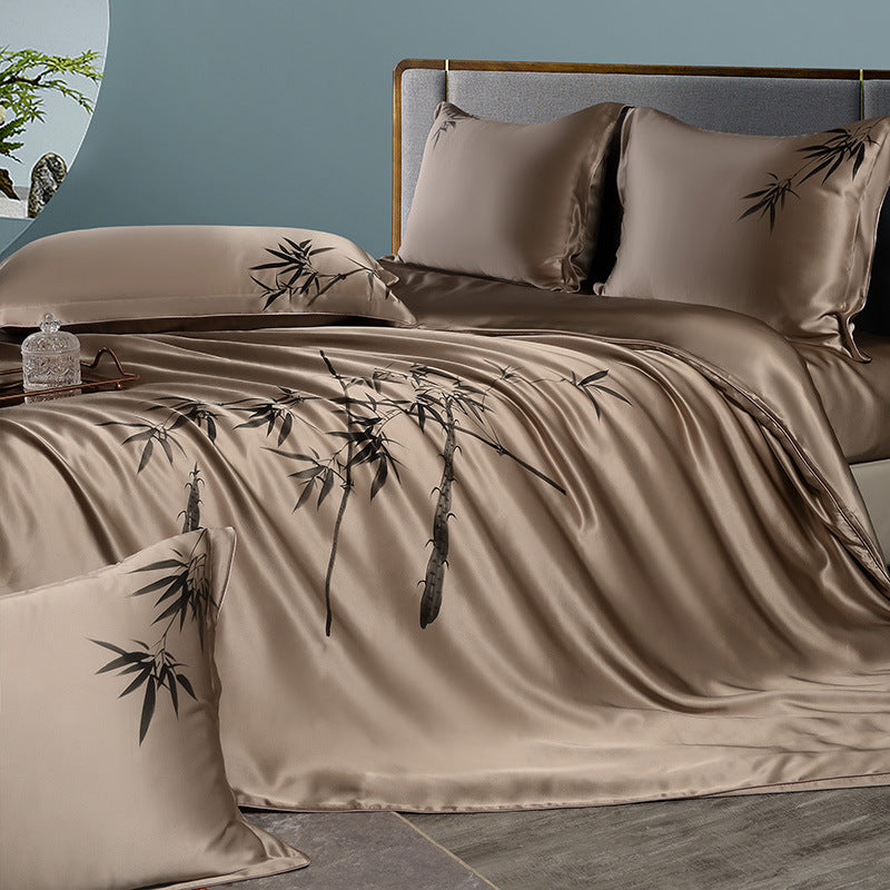 Beige silk bedding set with bamboo design on a bed against a blue wall.