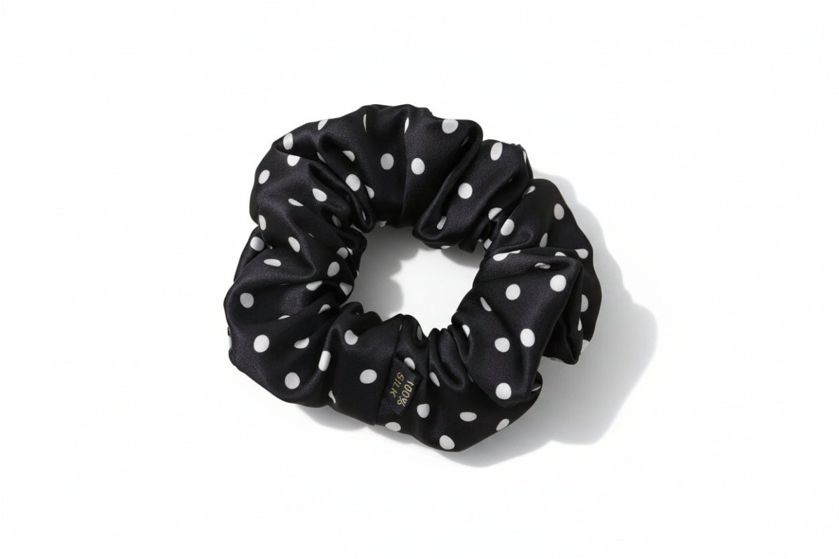 Black silk scrunchie with white polka dots on a light beige surface