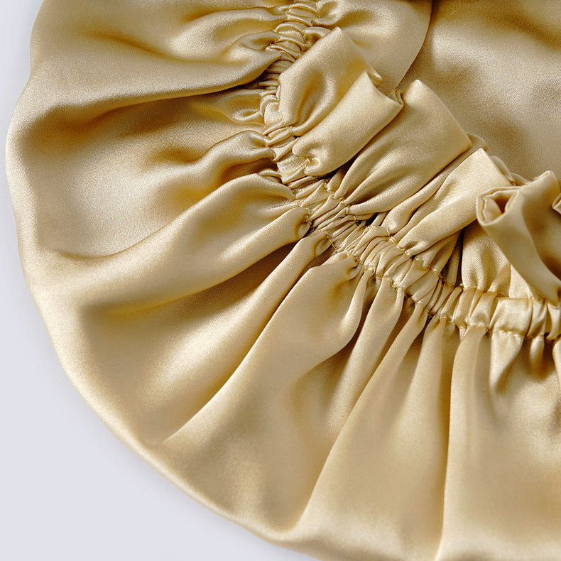 Close-up of a champagne gold silk bonnet with gathers on a white background