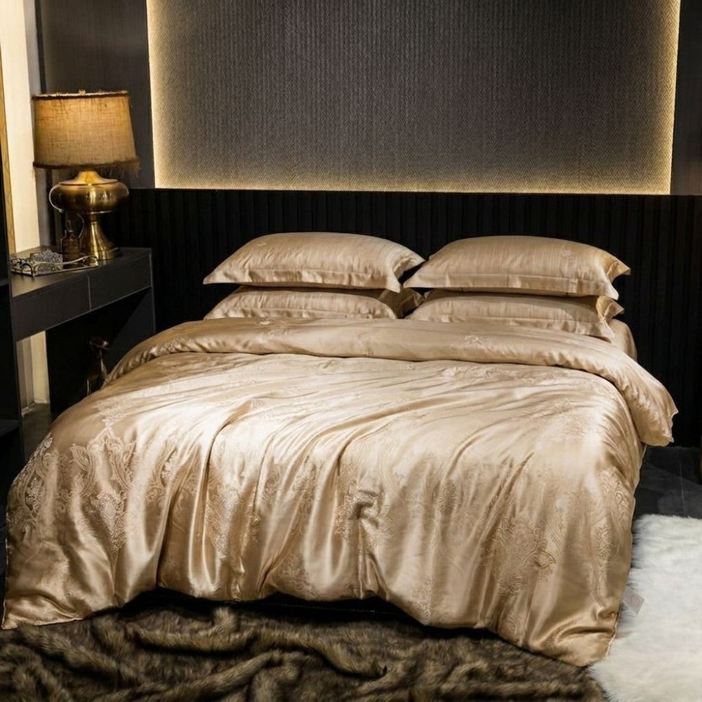 Champagne gold silk bedding set on a bed in a bedroom setting with a lamp and dark walls.
