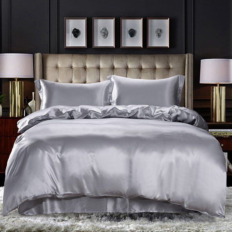 Gray silk duvet cover on a bed with a dark wall and framed pictures in the background.