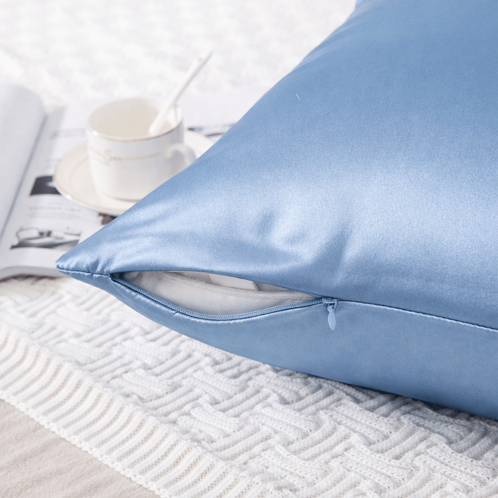 Light blue silk pillowcase on a textured white surface with a cup and magazine in the background.
