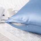 Light blue silk pillowcase on a textured white surface with a cup and magazine in the background.