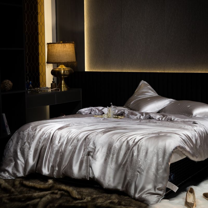 Luxurious bedroom with a bed featuring a silk duvet cover and pillows, nightstand with lamp.