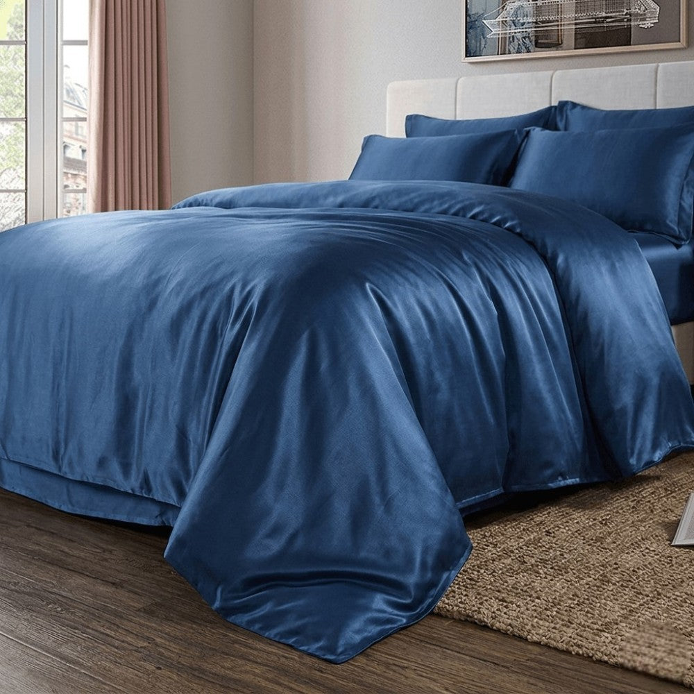 Blue silk bedding set on a bed in a bedroom with a window and curtains.
