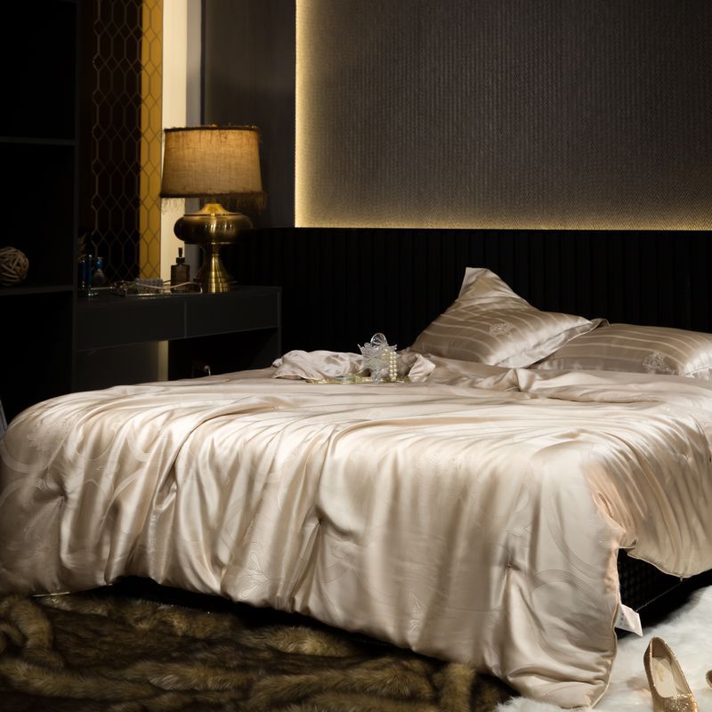Neatly made bed with a silk duvet cover in a dimly lit bedroom.