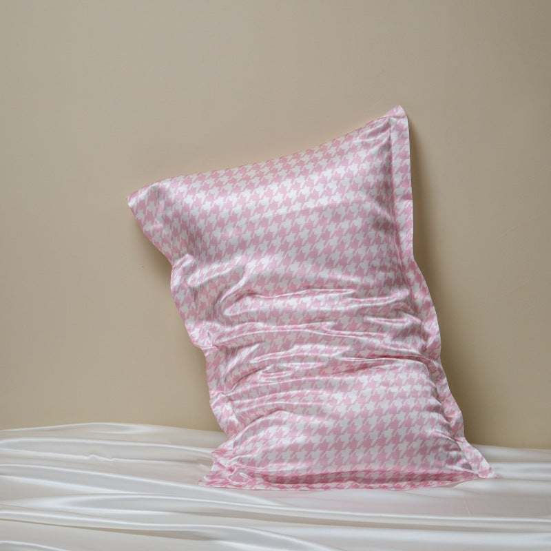 Pink houndstooth silk pillowcase on a white bed against a beige wall