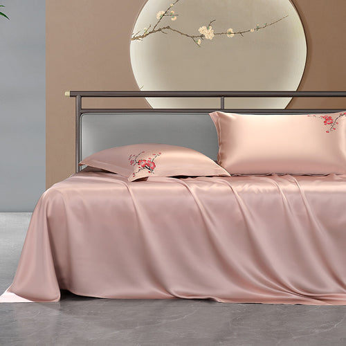 Pink silk bedding set with floral embroidery on a bed in a bedroom setting.