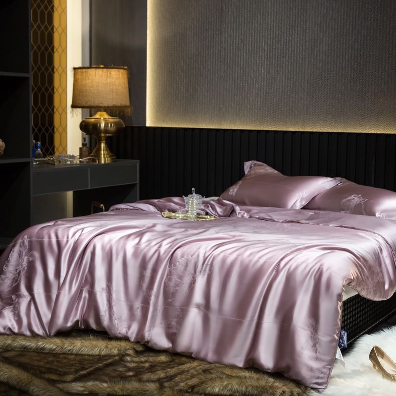 Purple silk duvet cover on a bed in a bedroom with a lamp and decor.