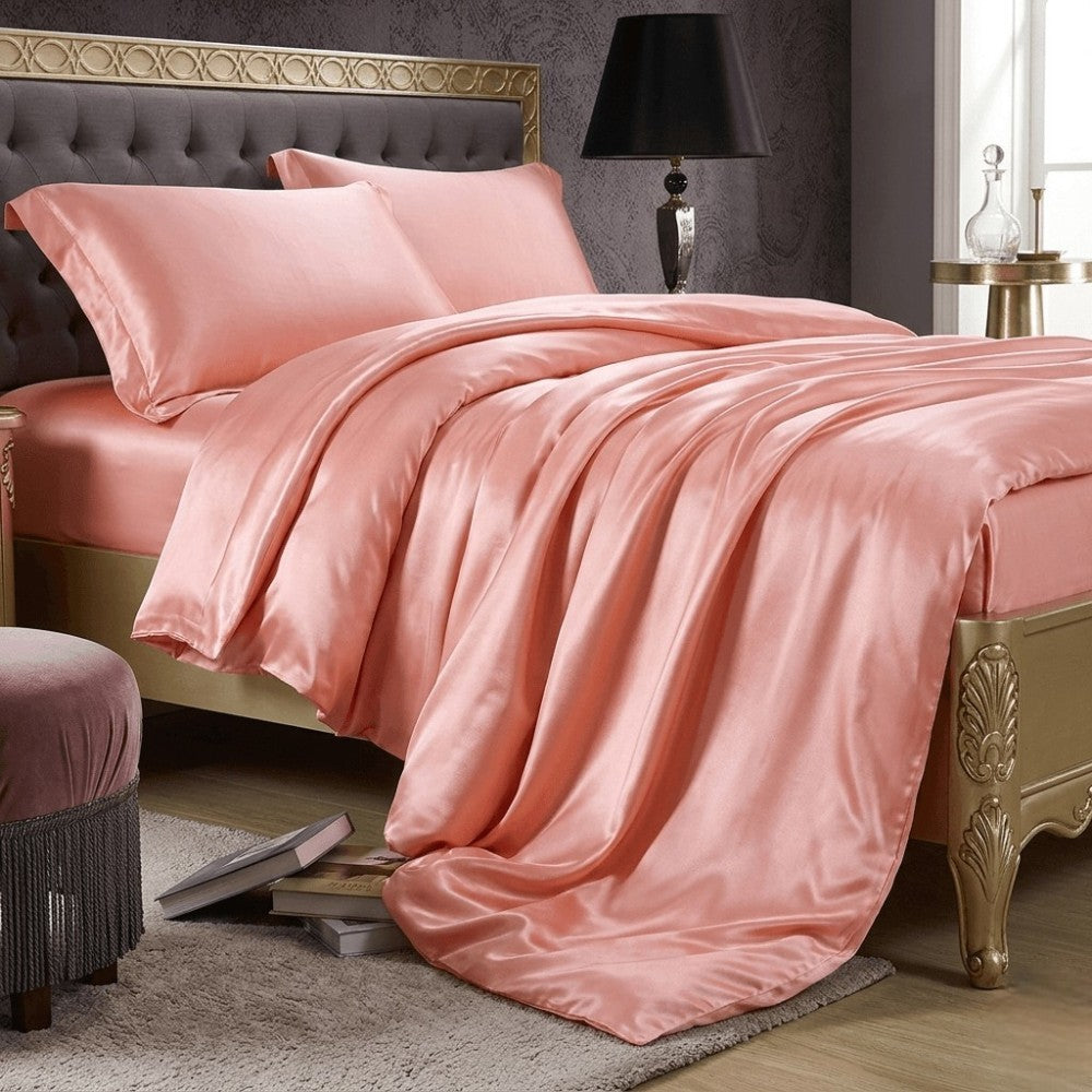 Pink silk bedding set on a bed with a decorative headboard and lamp.