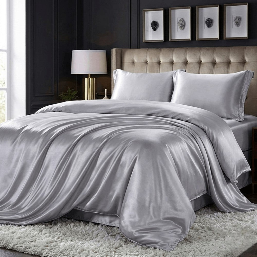 Gray silk comforter on a bed in a bedroom setting with a lamp and framed pictures.
