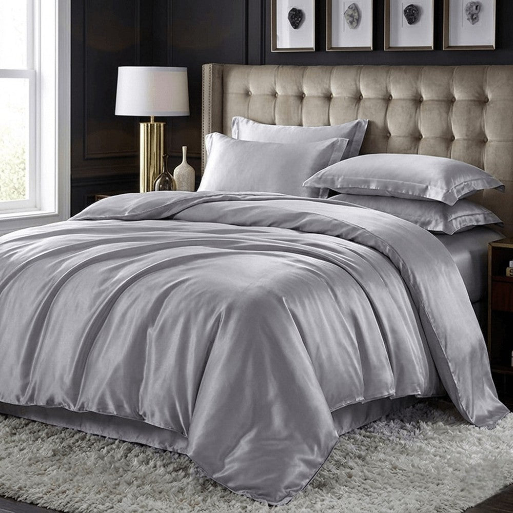 Gray silk bedding set on a bed with a tufted headboard in a bedroom setting.