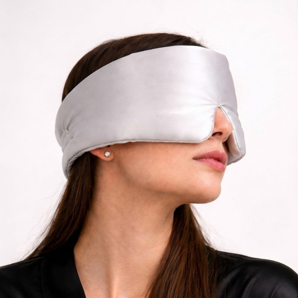 Woman wearing a silver grey silk sleep mask on a plain background