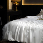 White silk duvet cover with floral patterns on a dark bed in a dimly lit room.