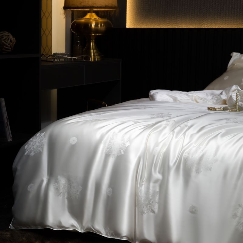 White silk duvet cover with floral patterns on a dark bed in a dimly lit room.