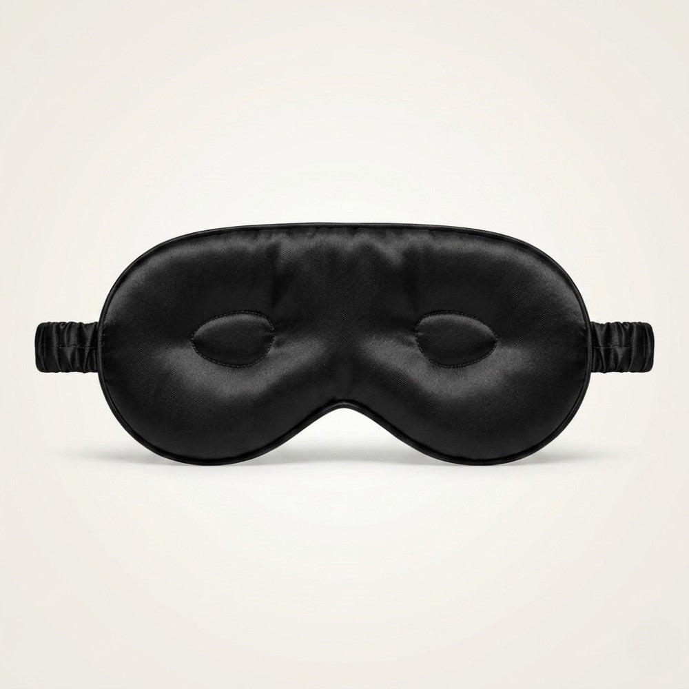 Black silk sleep mask with eye cups on a light beige background