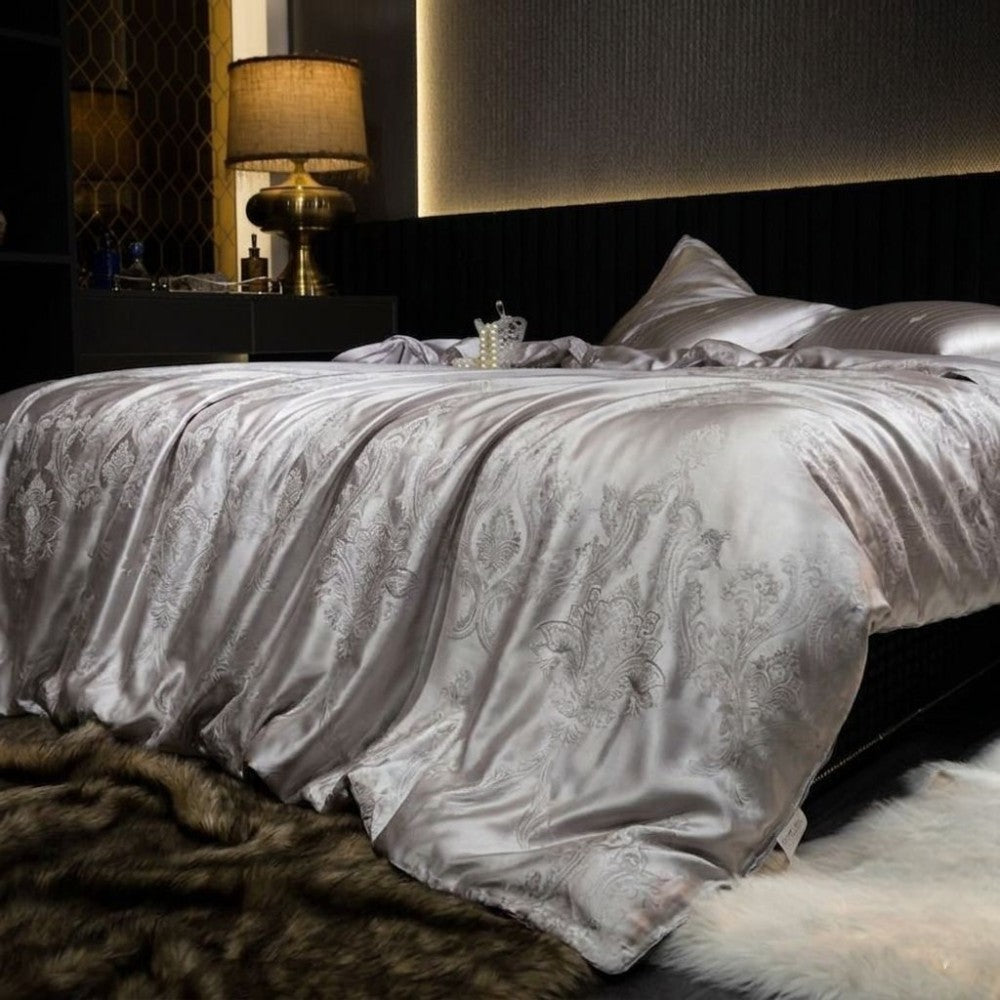 Luxurious bed with silver damask bedding in a dimly lit bedroom.