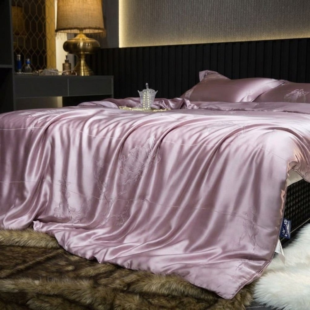 Light purple silk bedding set on a bed in a bedroom setting with a lamp and decorative items.