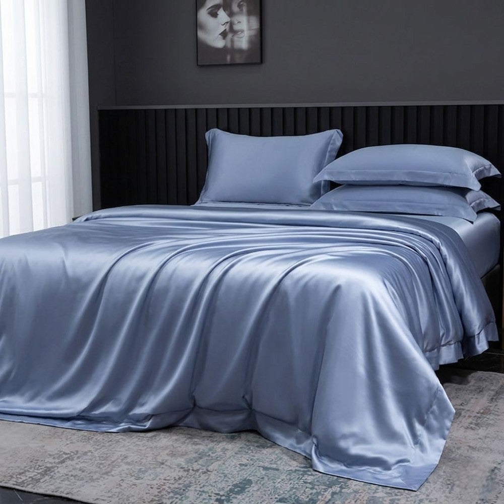 Blue silk bedding set on a bed in a bedroom with a dark wall and framed picture.