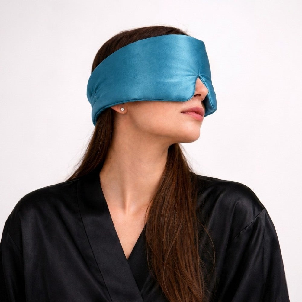 Woman wearing a blue silk sleep mask against a white background