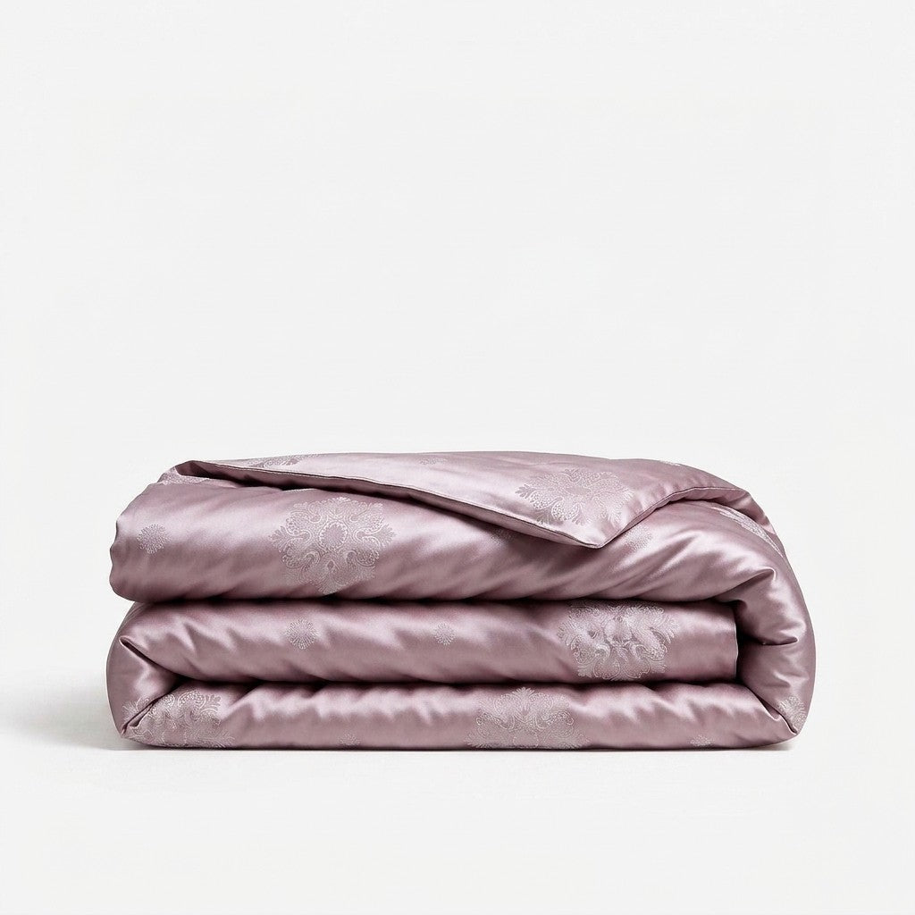 A folded light purple silk duvet cover with a subtle tonal damask pattern, displayed on a clean white background.