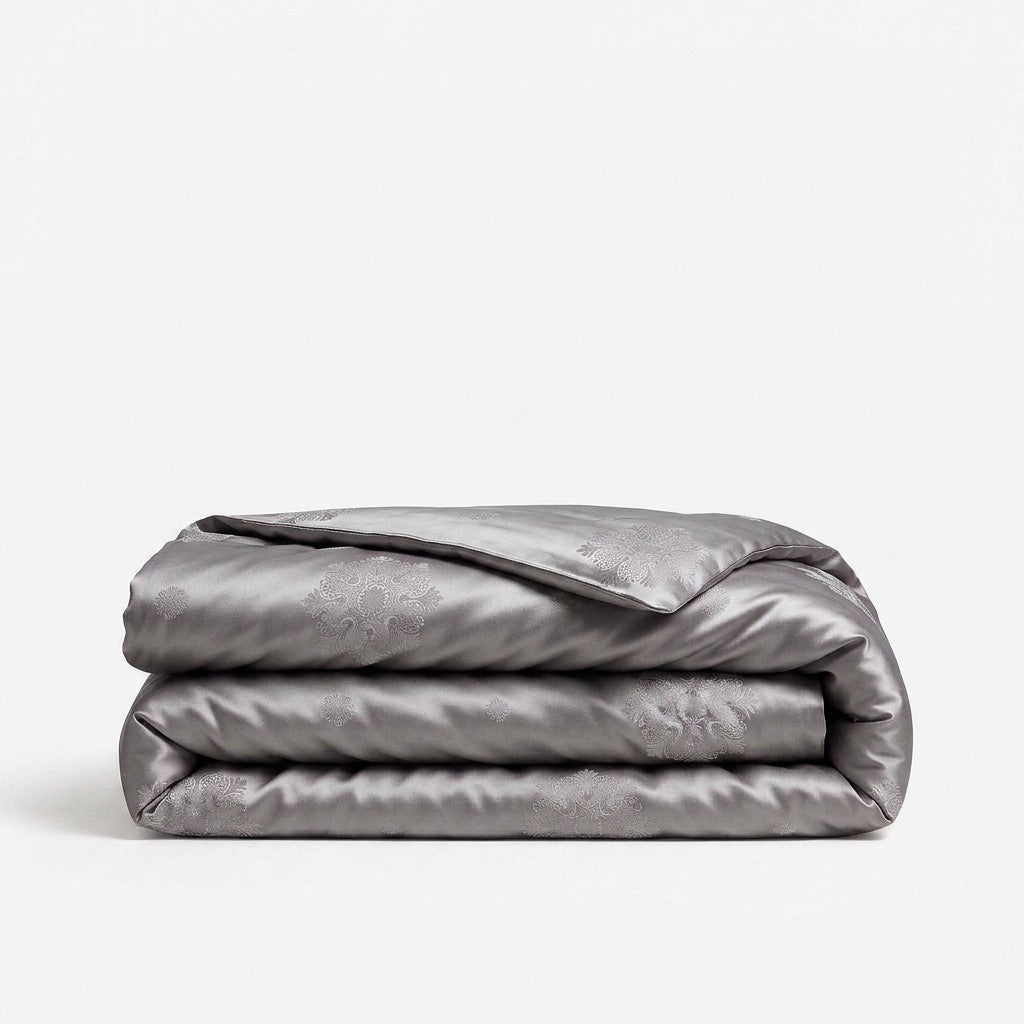 A folded gray silk duvet cover, featuring a subtle damask floral pattern.
