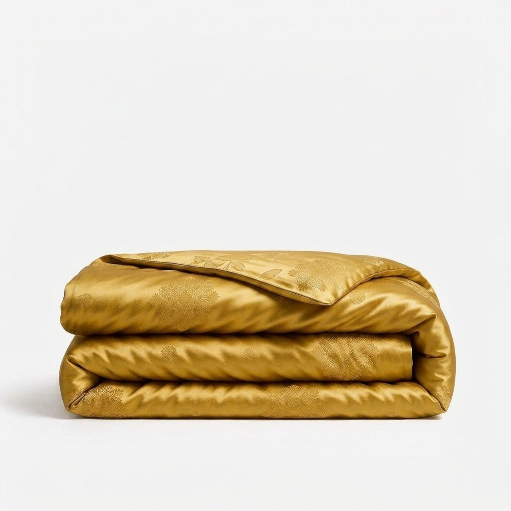 A folded golden-yellow silk duvet cover with a subtle woven pattern, displayed on a clean white background