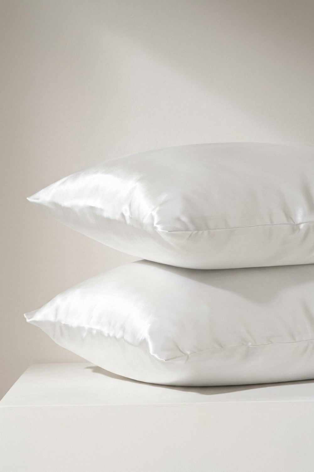 Two white silk pillowcases stacked on a light gray background